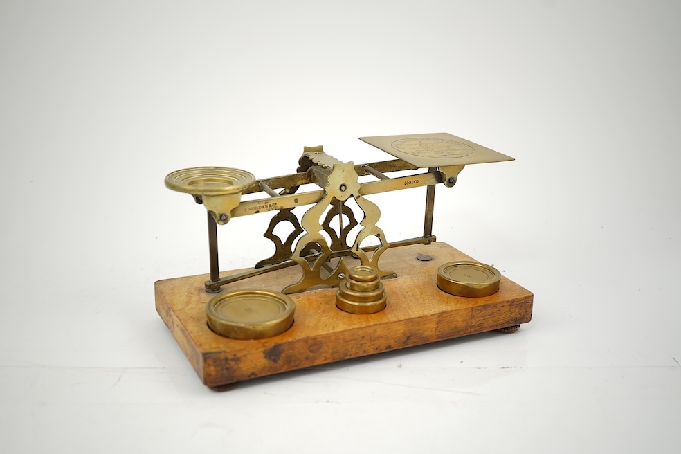 A Sampson Mordan & Co. set of brass postal scales on an oak base with weights, 27cm wide, with engraved prices for Inland Letter Post, etc.